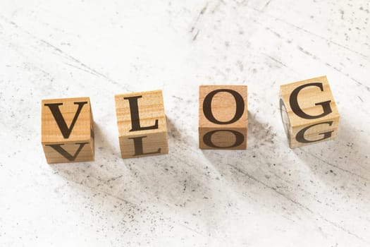 Four wooden cubes with word VLOG (meaning Video Blog) on white working board.