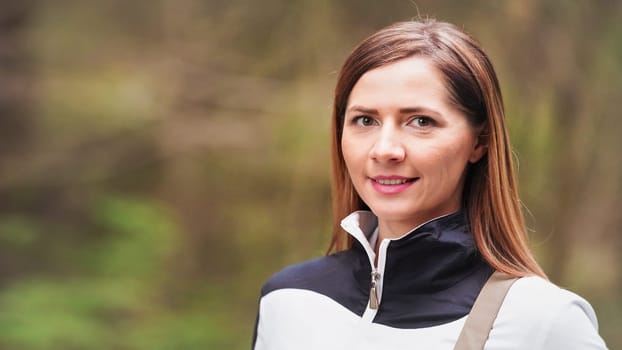 Portrait of young woman in white sport jacket, blurred forest background, space for text left side