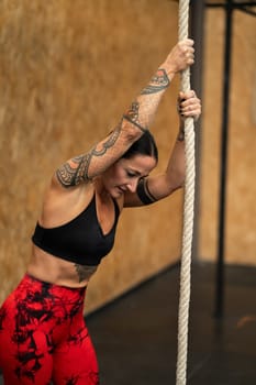 Tired sportive woman about to climb a rope in a gym