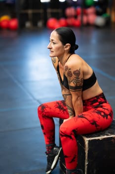 Vertical photo of a mature fit woman sitting on a box resting after training in a gym