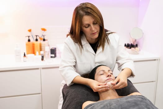 Young female therapist massaging face of woman while relaxing in beauty salon during facial treatment