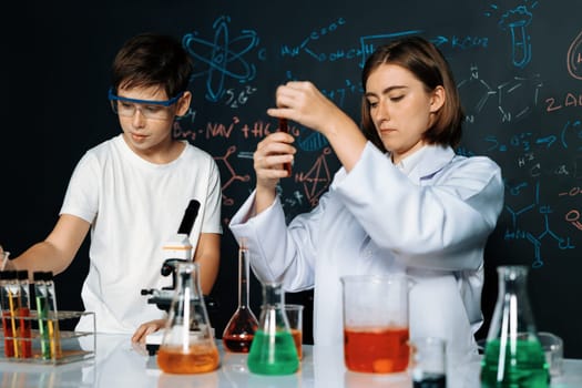 Teacher support schoolboy in laboratory. Schoolboy and teacher stand and experiment about science of chemistry in STEM class using liquid in glass container. Instructor mixing solution. Erudition.
