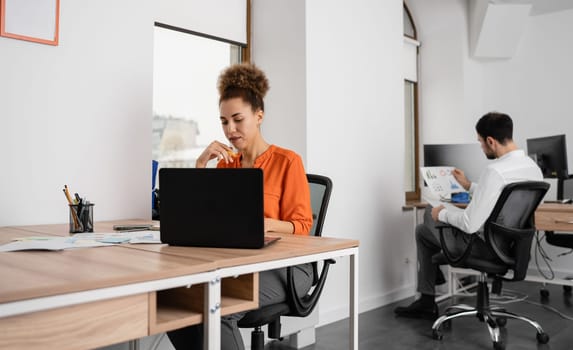 Two young businesspeople smiling while working with wireless technology in a modern workspace.