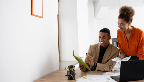 Two young businesspeople smiling while working with wireless technology in a modern workspace.