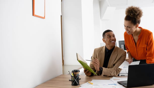 Two young businesspeople smiling while working with wireless technology in a modern workspace.