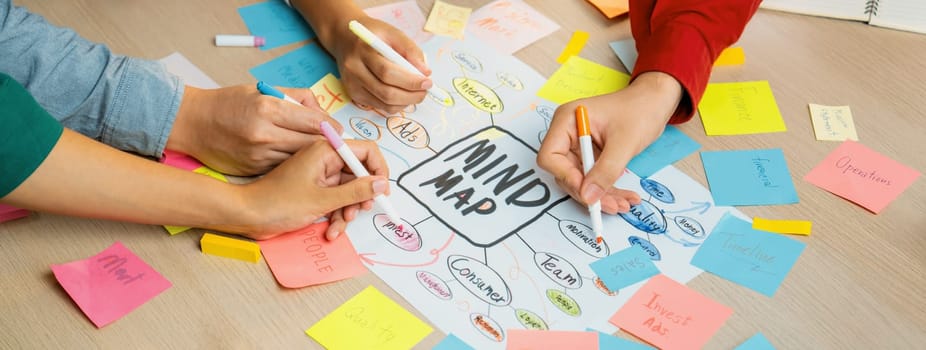 Professional startup group share creative marketing idea by using mind map. Young skilled business people brainstorm business plan while writing sticky notes. Focus on hand. Closeup. Variegated.