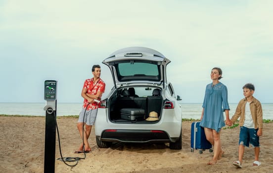 Family vacation trip traveling by the beach with electric car, lovely family taking luggage out while charging EV car battery with clean energy. Alternative family travel by eco-friendly car.Perpetual