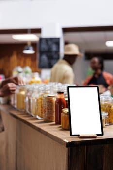 Close-up of phone tablet displaying an isolated copyspace template is seen at an eco friendly food shop. Focused image of a digital device with an empty mockup display, placed near bio-food products.