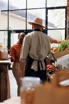 Shopkeeper providing expert advice to diverse couple as they shop for fresh, healthy, and natural groceries. Store emphasizes eco-friendly options, promoting small business that values sustainability.