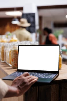 Detailed view of a digital laptop showing an isolated copyspace mockup template in an eco friendly supermarket. Close-up of african american person using minicomputer with blank white screen display.