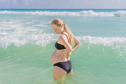 In the sea, a pregnant woman experiences a moment of discomfort as she stands, gently tending to her back, highlighting the challenges of back pain during pregnancy.