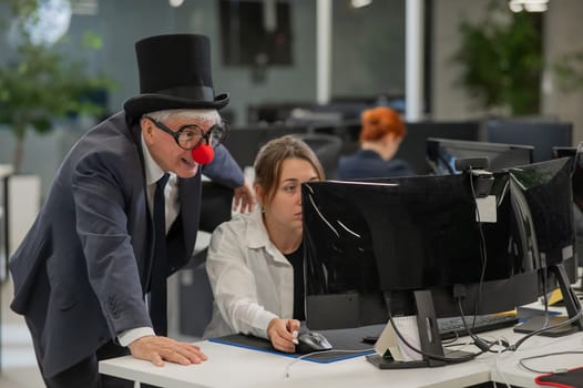 Caucasian woman works at the computer. Elderly man in clown costume in office
