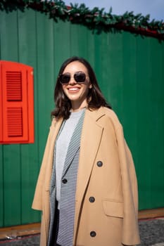 Happy caucasian girl walking Christmas holiday winter day in European city. Brunette woman wears stylish jacket, coat and sunglasses. Positive emotions lifestyle concept