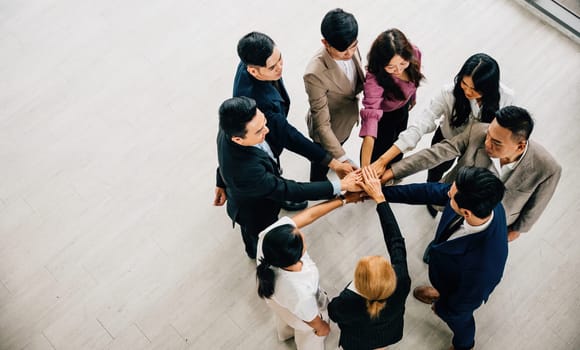 From above, four diverse colleagues form a unity circle, holding hands to create a symbolic stack. This represents teamwork, trust, and global success in business.