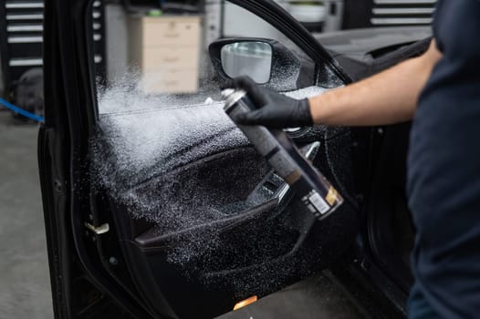 A man sprays cleaning foam on the interior of a car