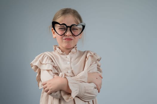 Portrait of a cute little girl grimacing wearing heart-shaped glasses on a white background