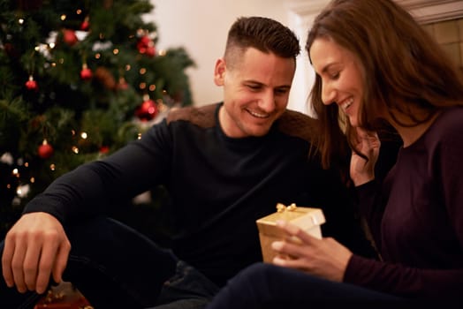 Couple, gift and Christmas in home with giving, love and support together with present. Celebration, holiday and tree with smile and happy with marriage in a house with romance and relationship.