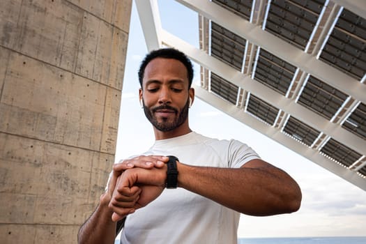 African American man checking pulse in smart watch. Black male athlete with wireless earphones using smart watch to put on music. Sport and technology concept.