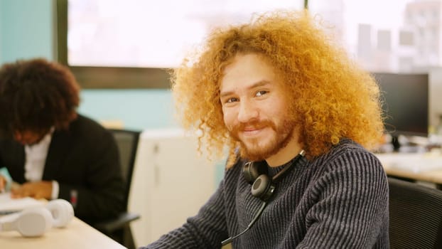Modern man with curly hair smiling while working in coworking
