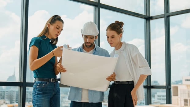 Professional architect engineer team talking, sharing, brainstorming about design while manager hold at project plan. Young architect holding plan while manager listen and point at plan. Tracery