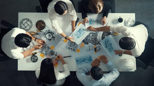 Top down aerial view of smart engineer team working together to design turbine engine. Professional technician discussing about jet engine construction while pointing at part of engine. Alimentation.