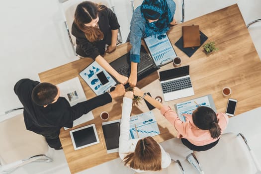 Businessmen and businesswomen joining hands in group meeting at multicultural office room showing teamwork, support and unity in business. Diversity workplace and corporate people working concept. uds