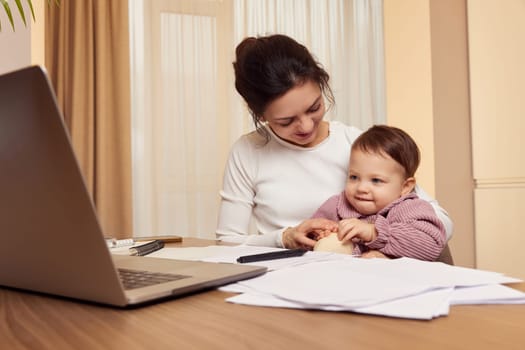 Cheerful pretty businesswoman working at home with her little child girl