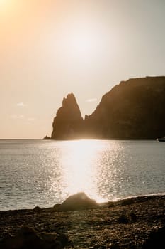 A red burning sunset with the silhouette of a cliff over the sea. Abstract nature summer or spring ocean sea background. Small waves on golden warm water surface with bokeh lights from sun.