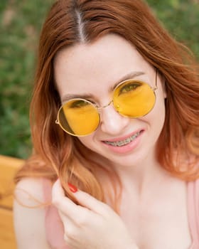 Beautiful young woman in yellow sunglasses smiling showing off braces on her teeth. Vertical photo