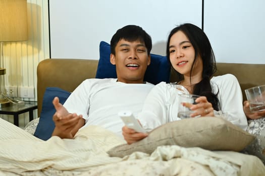 Carefree young couple with remote control lying in bed at home and watching tv.