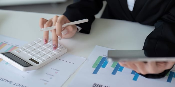 Finance concept. Close up businesswoman hold a graph pen and writing report, and memo, and analyzing business documents with a laptop computer.