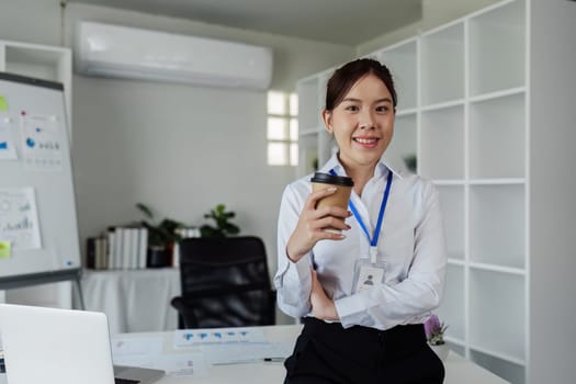 successful business woman standing in front of desk hold coffee cup to relax and look confident looking camera.