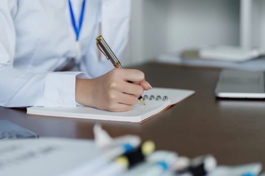 A woman is writing in a notebook with a pen. She is wearing a white shirt and has a blue lanyard. The scene suggests a professional setting