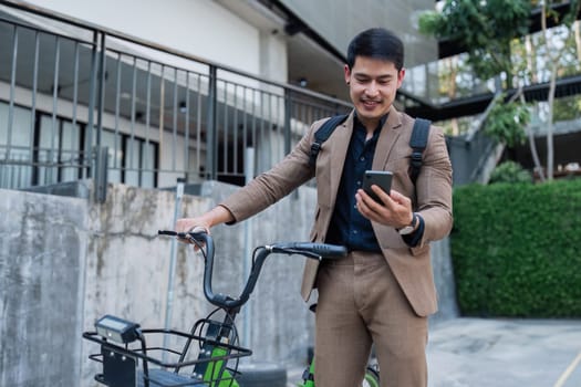 A man in a suit is standing next to a bicycle with a basket on it. He is looking at his cell phone