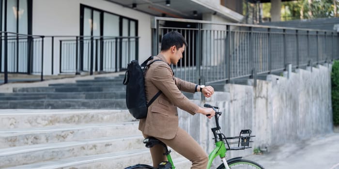 A man in a suit is riding a green bike with a basket. He is wearing a watch and a backpack