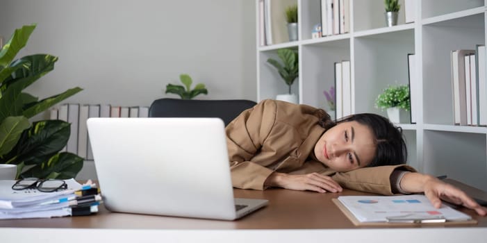 Asian businesswoman feeling tired and stressed over an unsuccessful business while working in a home office decorated with soothing green plants..