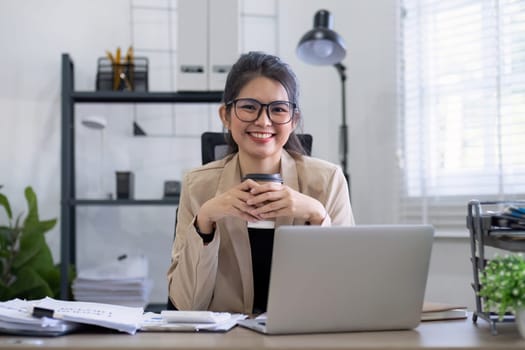 Asian businesswoman or accountant happily sitting and working with laptop on finance and business administration. On the desk in the office decorated with green plants..