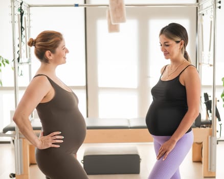 Two pregnant women communicate in a fitness club. Pilates for expectant mothers