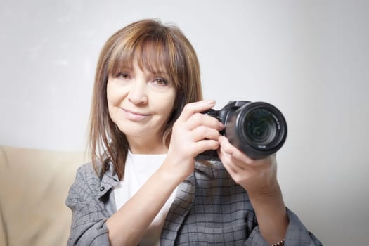 Senior old elderly woman with black camera with a large lens indoors in the studio. Professional photographer. Age Hobby