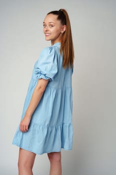 Young happy smiling woman in a light blue dress on a gray background close up