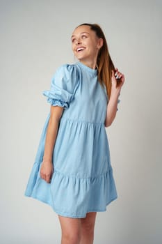 Young happy smiling woman in a light blue dress on a gray background close up