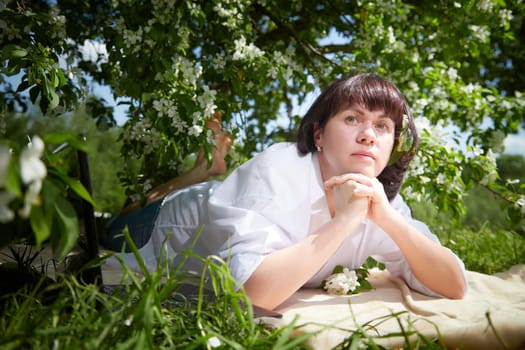 Girl Relaxing, sleeping near Blossoming apple Tree on Sunny Day. Portrait of Middle aged woman enjoying nature surrounded near white blossoms