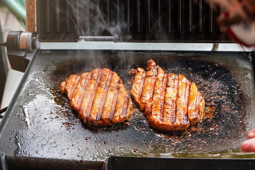 Two pork cutlets steaks grilled on electric grill, smoke visible above cooked meat