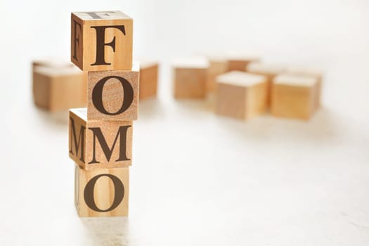 Four wooden cubes arranged in stack with letters FOMO (meaning Fear of Missing Out) on them, space for text / image at down right corner