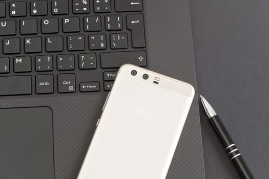 Black laptop keyboard, mobile phone and pen on gray table - view from above