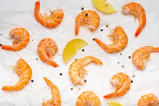Roasted or grilled shrimps with seasonings and fresh lemon wedges top view on baking paper, healthy snack or appetizer. Seafood barbecue.