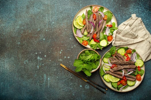 Two plates with traditional Thai beef salad with vegetables and mint top view served on rustic concrete background, healthy exotic asian meal, space for text.