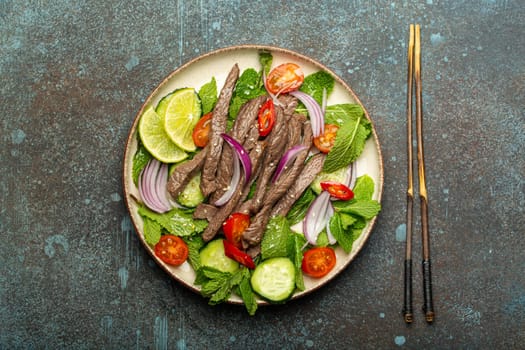 Plate with traditional Thai beef salad with vegetables and mint top view served on rustic concrete stone background, healthy exotic asian meal.