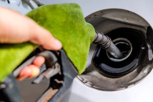 Close up image of hand refilling a car with fuel at a gas station, green fuel nozzle,energy concept