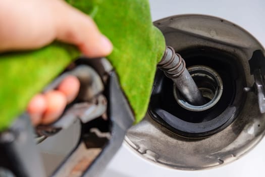 Close up image of hand refilling a car with fuel at a gas station, green fuel nozzle,energy concept